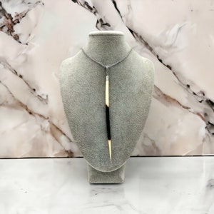 May include: A long, thin, black and white pendant necklace with a silver chain. The pendant is made of natural materials and has a unique, organic shape.