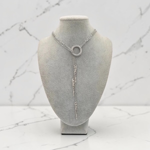 May include: A silver-toned lariat necklace featuring a circular ring pendant connected to multiple delicate chains. Three slender, pointed metal spikes hang from the chains, creating a layered, vertical drop design that rests against the neck form.