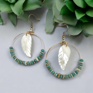 May include: Gold hoop earrings with turquoise and white beads and a white shell leaf charm.