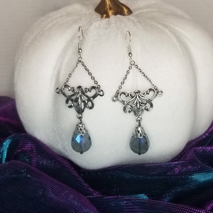 May include: Silver dangle earrings with a teardrop-shaped blue crystal pendant. The earrings feature a delicate filigree design.