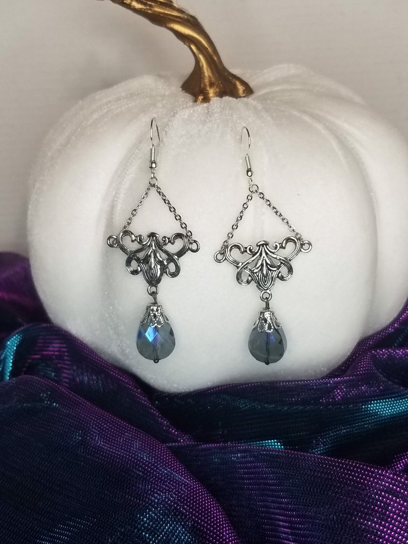 May include: Silver dangle earrings with a teardrop-shaped blue crystal pendant. The earrings feature a delicate filigree design.