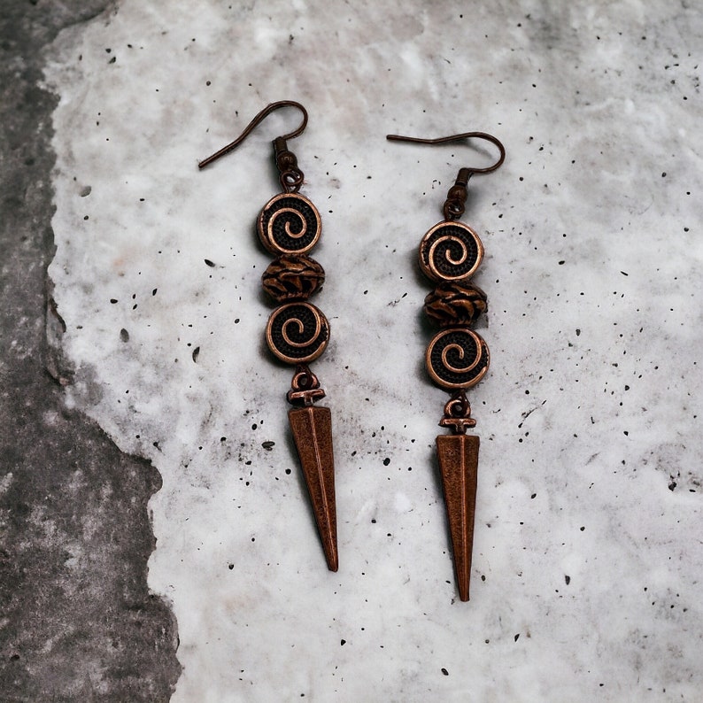 May include: A pair of long, bronze earrings with a pointed tip and three decorative beads. Each bead has a spiral design.