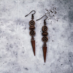 May include: A pair of long, copper-colored earrings with a pointed tip and three spiral-shaped beads.