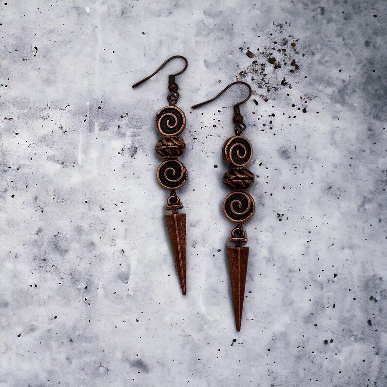 May include: A pair of long, copper-colored earrings with a pointed tip and three spiral-shaped beads.