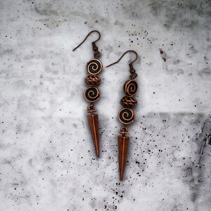 May include: A pair of long, copper-colored earrings with a pointed tip and three black and copper beads with a spiral design.