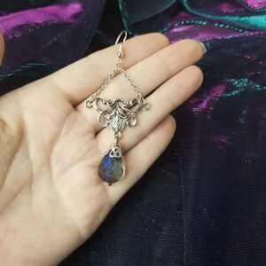 May include: Silver dangle earring with a teardrop-shaped iridescent blue glass bead hanging from a silver filigree design.