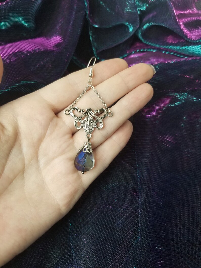 May include: Silver dangle earring with a teardrop-shaped iridescent blue glass bead hanging from a silver filigree design.