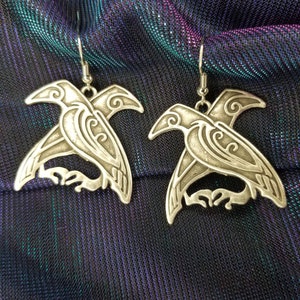 May include: A pair of silver earrings shaped like stylized ravens. The earrings have intricate details and a dangling design.
