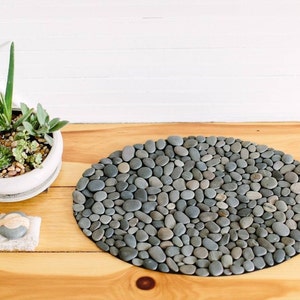 oval-shaped gray stone bath mat made of smooth, rounded pebbles.