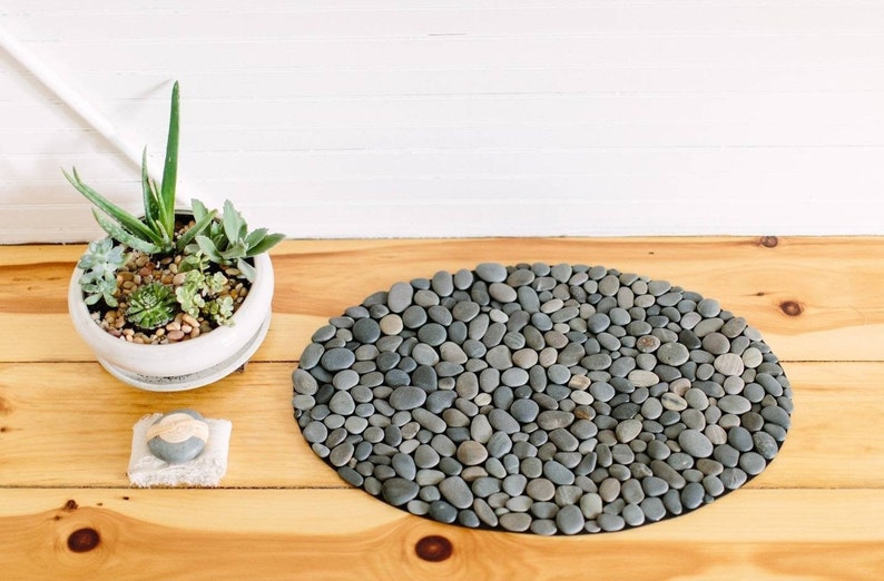 oval-shaped gray stone bath mat made of smooth, rounded pebbles.