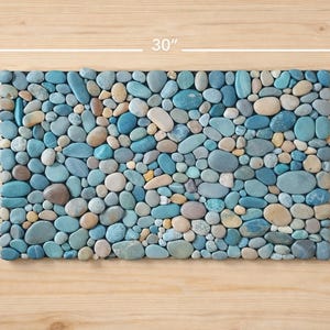 Pu&ograve; includere: Mosaico rettangolare realizzato con pietre lisce e arrotondate nei toni del blu, grigio e beige. Il mosaico misura 76 cm di lunghezza e 46 cm di larghezza, adatto come elemento decorativo o superficie funzionale.
