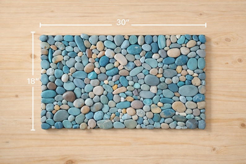 Pu&ograve; includere: Mosaico rettangolare realizzato con pietre lisce e arrotondate nei toni del blu, grigio e beige. Il mosaico misura 76 cm di lunghezza e 46 cm di larghezza, adatto come elemento decorativo o superficie funzionale.