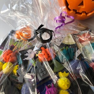 May include: A Halloween-themed gift basket wrapped in clear cellophane, tied with orange and black ribbons. The basket contains various Halloween-themed trinkets and a ceramic jack-o'-lantern.