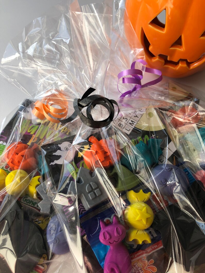 May include: A Halloween-themed gift basket wrapped in clear cellophane, tied with orange and black ribbons. The basket contains various Halloween-themed trinkets and a ceramic jack-o'-lantern.