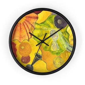 May include: A yellow, green, and orange wall clock with a black frame. The clock face features an abstract design with a variety of shapes and colors.