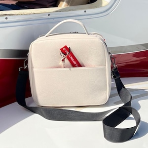 May include: A white leather crossbody bag with a black strap and a red keychain with the text "LOVE BEFORE FLY".