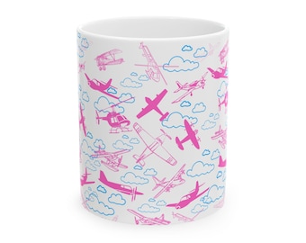 May include: White ceramic mug with a pink and blue pattern of airplanes and clouds. The airplanes are of different styles, including propeller planes, jets, and helicopters.