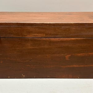 May include: A rectangular wooden box with a hinged lid. The box is stained a dark brown color, with visible wood grain and some wear. The hinges are metal. The box is likely used for storage.