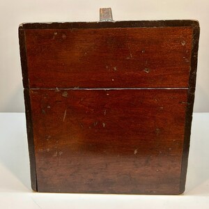 May include: A rectangular wooden box with a dark brown finish. The box has a hinged lid and a small metal clasp. The wood grain is visible, and the box appears to be vintage or antique.