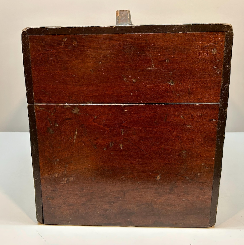 May include: A rectangular wooden box with a dark brown finish. The box has a hinged lid and a small metal clasp. The wood grain is visible, and the box appears to be vintage or antique.