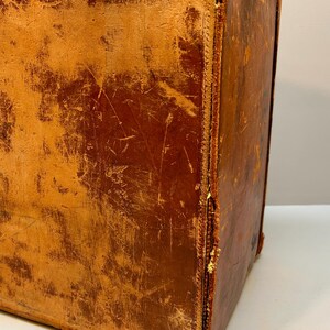 May include: A vintage, rectangular suitcase with a distressed, brown leather exterior. The corners and edges show wear and tear, with visible stitching and a slightly lighter color. The suitcase appears to be well-used and aged.