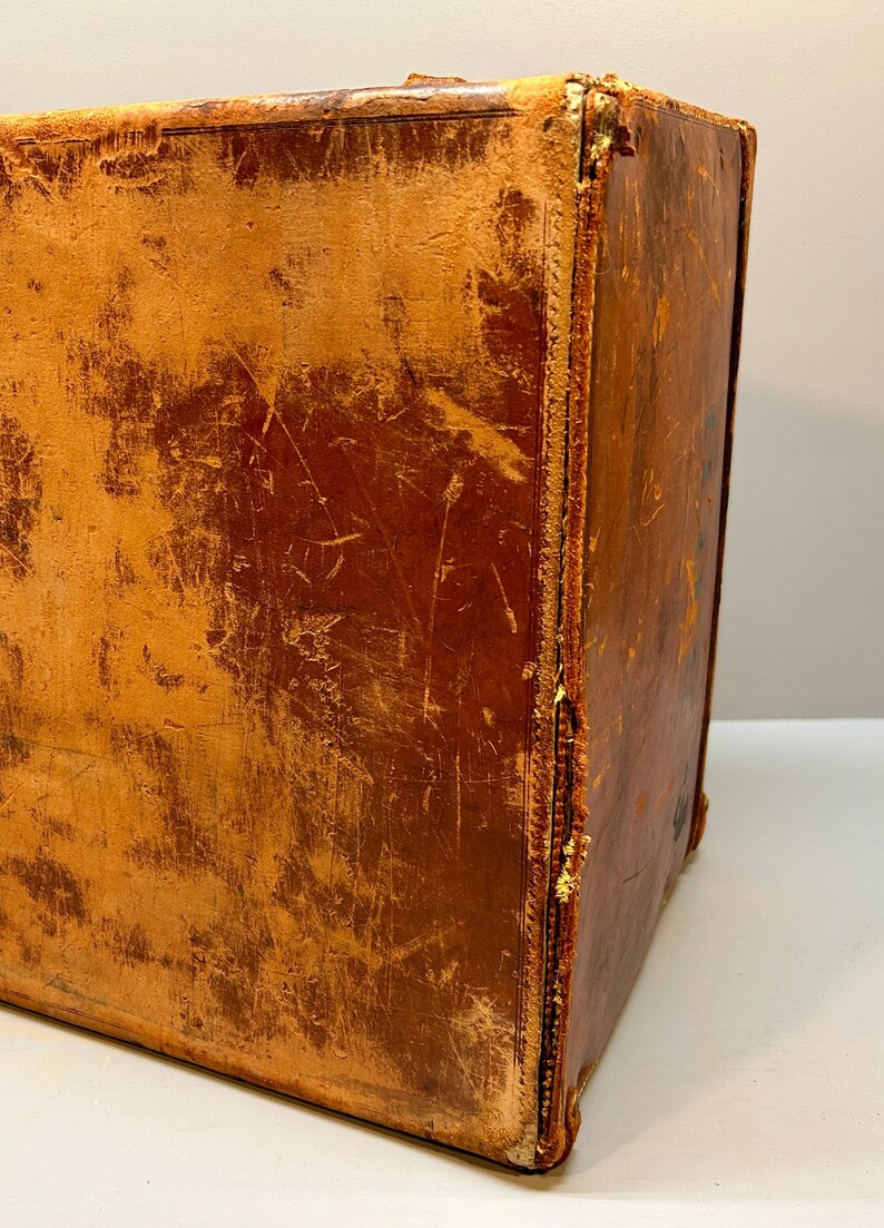 May include: A vintage, rectangular suitcase with a distressed, brown leather exterior. The corners and edges show wear and tear, with visible stitching and a slightly lighter color. The suitcase appears to be well-used and aged.