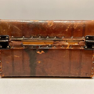 May include: A vintage brown leather suitcase with metal clasps and rivets. The suitcase has a diamond-shaped design on the front.