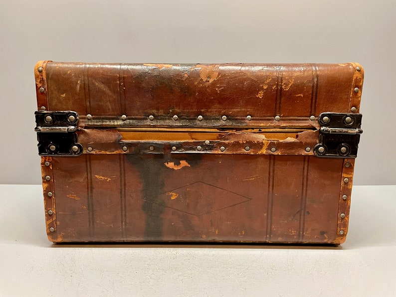 May include: A vintage brown leather suitcase with metal clasps and rivets. The suitcase has a diamond-shaped design on the front.