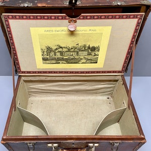 May include: An antique brown leather suitcase with brass hardware and a fabric lining. The inside of the suitcase has two compartments. The suitcase has a label that reads "AMES SWORD CO. CHICOPEE MASS."
