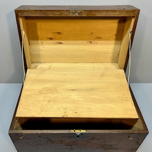 May include: An open, antique wooden chest with a hinged lid and a small interior shelf. The chest is made of dark brown wood with a lighter wood interior. The chest has a metal latch and hinges. The chest is empty.