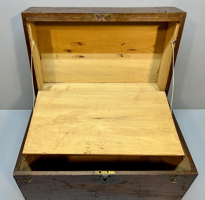 May include: An open, antique wooden chest with a hinged lid and a small interior shelf. The chest is made of dark brown wood with a lighter wood interior. The chest has a metal latch and hinges. The chest is empty.
