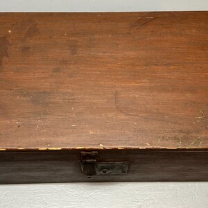 May include: A rectangular wooden box with a hinged lid and a metal clasp. The box is stained a dark brown color, showing the wood grain. The box appears to be vintage or antique, with some wear and tear visible on the surface.
