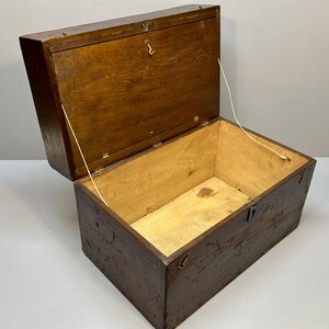 May include: An open, rectangular wooden chest with a hinged lid. The chest is stained a dark brown color, with lighter wood visible on the interior. The lid is held open by a string. The chest has metal hardware.