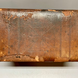 May include: A vintage leather-bound trunk with a decorative cross design. The trunk is brown and has metal studs around the edges.