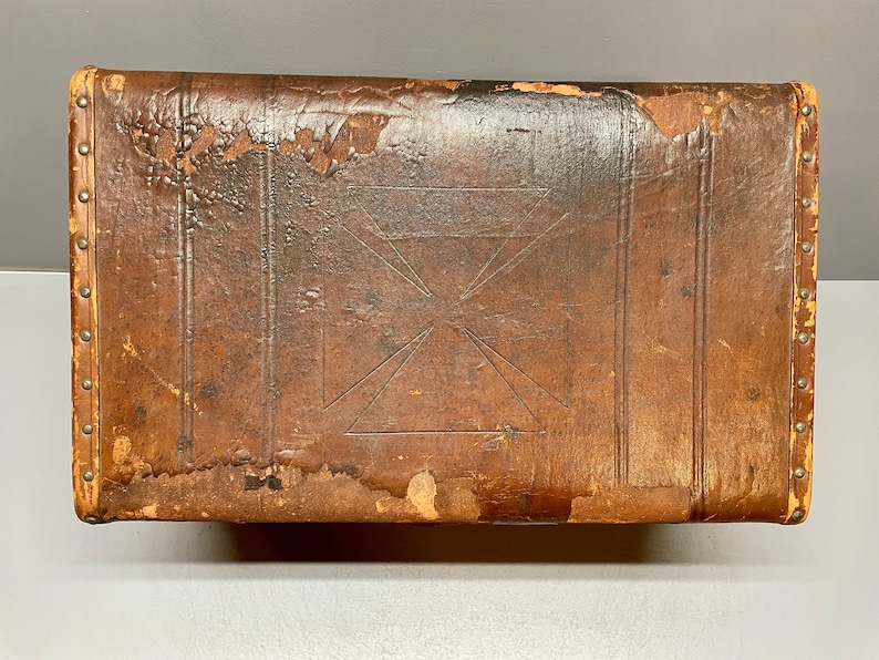 May include: A vintage leather-bound trunk with a decorative cross design. The trunk is brown and has metal studs around the edges.