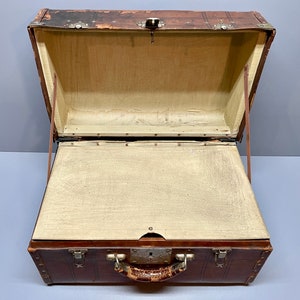 May include: A vintage brown leather suitcase with brass hardware and a leather handle. The suitcase is open and the inside is lined with a beige fabric.