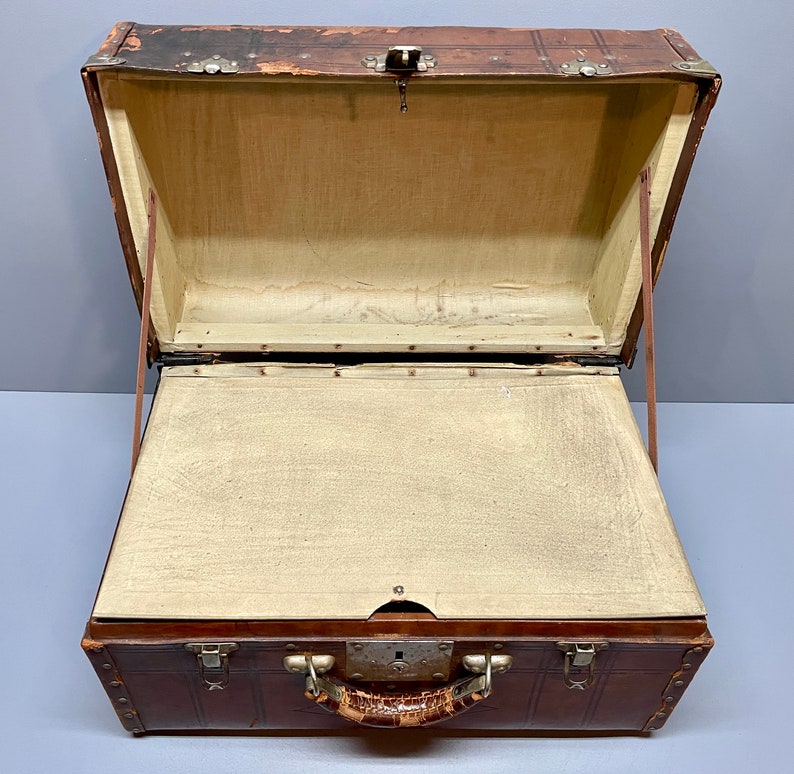 May include: A vintage brown leather suitcase with brass hardware and a leather handle. The suitcase is open and the inside is lined with a beige fabric.