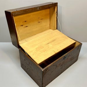 May include: An open, antique wooden chest with a hinged lid. The exterior is a dark brown, while the interior and lid are light-colored wood. The chest has a rectangular shape and a metal clasp.