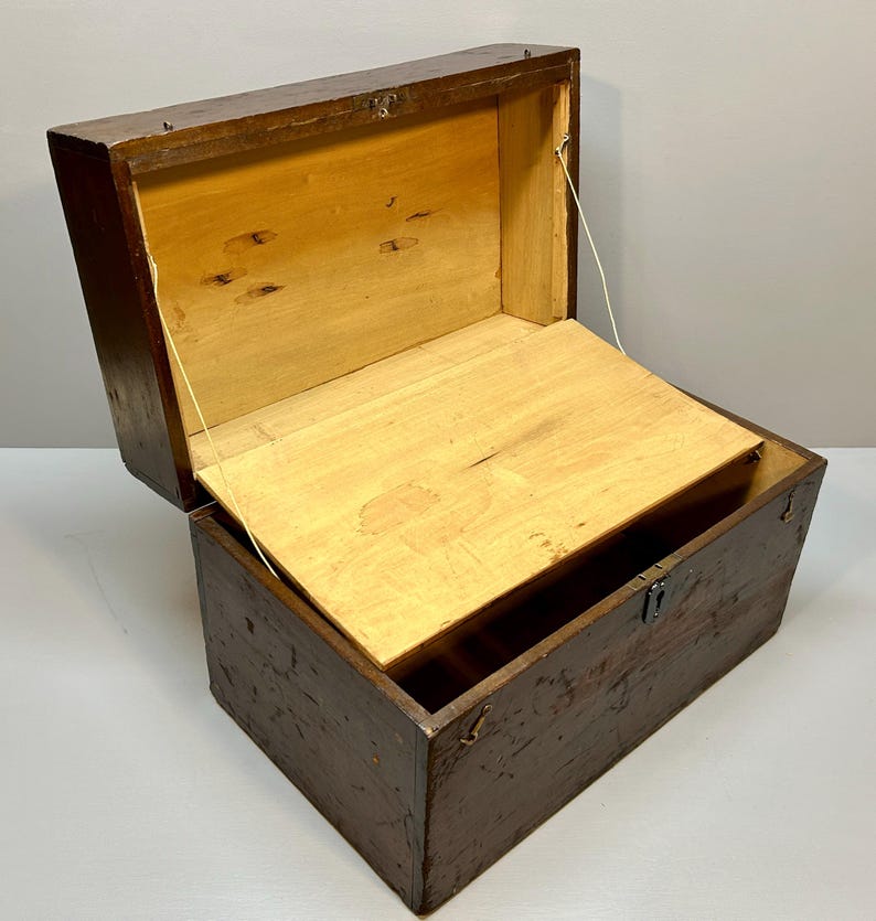 May include: An open, antique wooden chest with a hinged lid. The exterior is a dark brown, while the interior and lid are light-colored wood. The chest has a rectangular shape and a metal clasp.