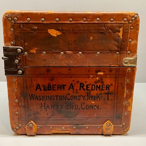 May include: A vintage brown leather suitcase with metal accents and the text "ALBERT A. REDMER WASHINGTON COMDY. N.Y.K. T. HARTFORD. CONN." printed on the front.