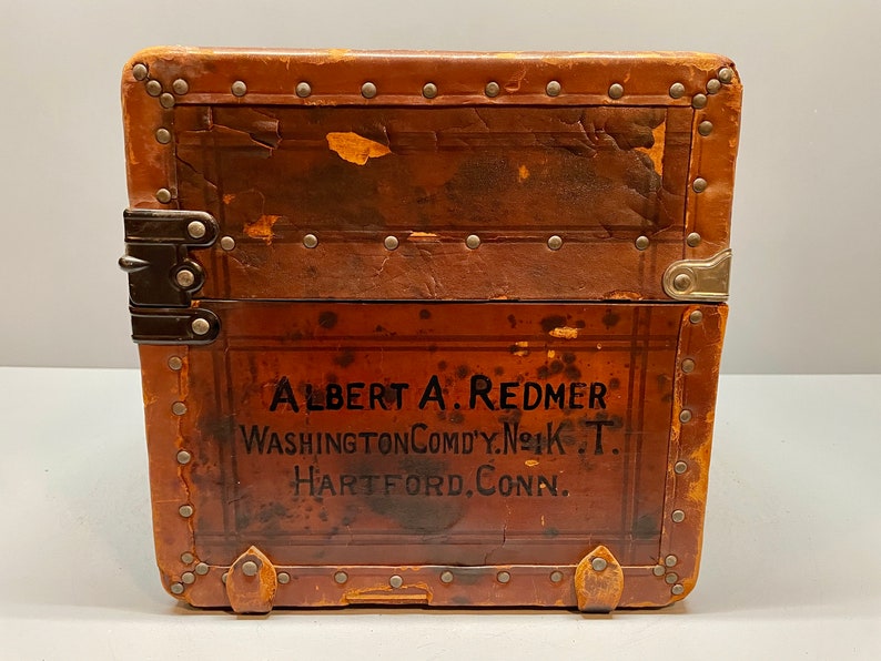 May include: A vintage brown leather suitcase with metal accents and the text "ALBERT A. REDMER WASHINGTON COMDY. N.Y.K. T. HARTFORD. CONN." printed on the front.