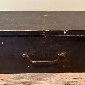 May include: A black wooden box with a metal handle and brass clasps. The box has a worn, vintage look.
