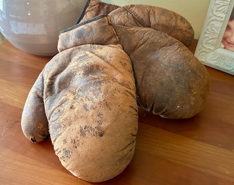 May include: A pair of vintage brown leather boxing gloves with a worn and distressed look.
