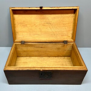 May include: An open, antique wooden chest with a dark brown exterior and a light brown interior. The lid is open, revealing the empty space inside. The chest has a metal latch and hinges. The wood grain is visible.