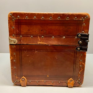 May include: A vintage brown leather suitcase with metal accents and a black latch. The suitcase has a worn and distressed look, suggesting it has been well-loved and traveled with.