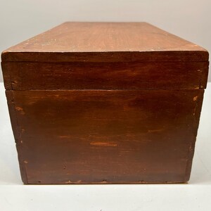 May include: A rectangular wooden box with a dark brown finish. The box has a simple design with a flat top and sides. The wood grain is visible, adding texture to the surface. The box appears to be well-constructed and sturdy.
