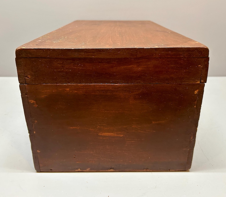 May include: A rectangular wooden box with a dark brown finish. The box has a simple design with a flat top and sides. The wood grain is visible, adding texture to the surface. The box appears to be well-constructed and sturdy.