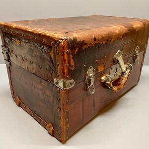 May include: A vintage brown leather suitcase with metal hardware and a lock. The suitcase has a worn and distressed look, giving it a rustic charm.