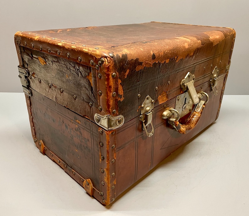 May include: A vintage brown leather suitcase with metal hardware and a lock. The suitcase has a worn and distressed look, giving it a rustic charm.