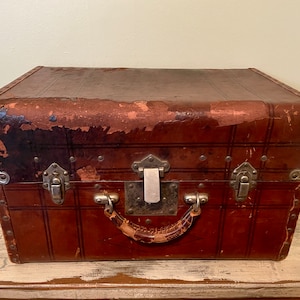 May include: A vintage brown leather suitcase with metal clasps and a leather handle. The suitcase has a worn and distressed look, with some of the leather peeling off.